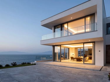 Wide architectural shot of a modern luxury villa in Izmir at dusk, featuring a sleek, closed glass balcony system overlooking the Aegean sea, clean lines, warm interior lighting glowing through the glass, high-end aluminum frames.
