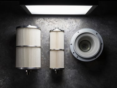 Flat-lay overhead of inline compressed air line filter assemblies on a dark steel surface, bowl and element separated to show internal structure, studio strobe from above