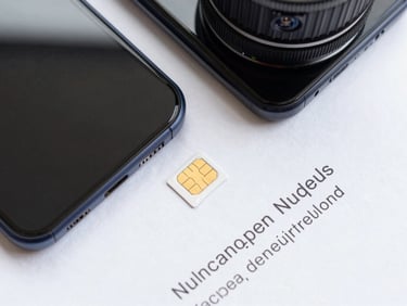 Overhead flat-lay of a smartphone next to a SIM card and a printed unlock code on white paper, bright even studio lighting, clean and technical composition