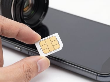 Macro close-up of a nano-SIM card being held between two fingers over a phone tray, bright daylight studio lighting, white background, sharp technical focus