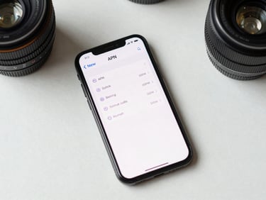 Overhead flat-lay of a smartphone displaying network APN settings menu on a clean white desk, bright even studio lighting, precise technical framing