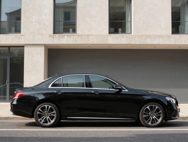 Profile shot of a black Mercedes-Benz E-Class sedan parked on a clean street in Aix-en-Provence, modern architectural backdrop, bright daylight