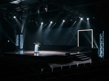 Cinematic wide-angle shot of an empty, perfectly lit corporate keynote stage, crisp spotlights casting sharp lines, deep rich shadows, 35mm.