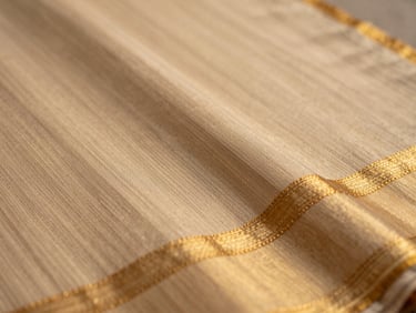 Close-up of handwoven Chanderi saree texture, showing the delicate gold zari borders and soft weave catching warm natural light, shallow depth of field.