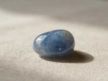 A single raw blue chalcedony stone resting on a piece of rough linen under soft morning daylight, shallow depth of field.