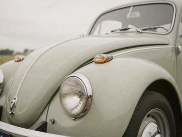 Tight detail shot of a vintage classic car fender and chrome headlight, soft overcast daylight, muted earth tones, sharp focus.