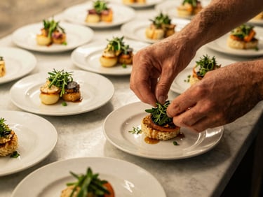Hands arranging herb garnishes on individual appetizer plates before a private dinner service, warm golden light, marble prep surface, fresh herbs visible mid-placement