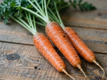 Close-up of raw organic carrots with soil on a rustic wooden table, soft natural daylight.