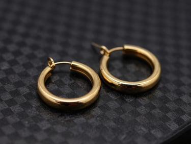 Extreme close-up of gold hoop earrings on a textured black carbon plate, highlights reflecting off polished metal, 85mm lens