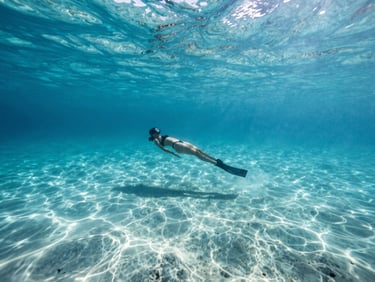 Wide-angle underwater landscape, natural sunbeams filtering through crystal-clear turquoise Caribbean water, a single diver suspended in weightless silence, cinematic lighting, premium underwater photography.