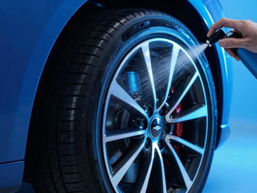 Sleek car tire being sprayed with detailing liquid, fine mist caught in sharp studio light, neon blue accent glow