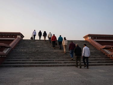 Wide environmental shot of pilgrims ascending temple steps in early morning ambient light, stone courtyard in foreground, group of travelers mid-journey, documentary style
