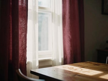 Warm domestic interior, soft linen curtains, sunlight filtering through a window onto a wooden table, 35mm