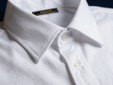 Macro photograph of a crisp white Egyptian cotton shirt collar, showing the immaculate stitching and premium fabric density