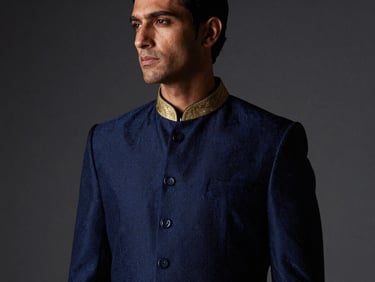 High-fashion editorial portrait of a man wearing a royal navy sherwani with subtle gold collar detailing, moody studio lighting