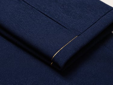 Macro photograph of folded navy blue wool trousers, showcasing the clean seam lines and premium fabric texture under dramatic side lighting.