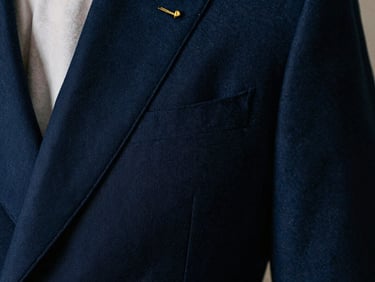 Close-up of a sharp navy blue suit lapel with gold lapel pin, dramatic side-shadow, medium format film aesthetic.