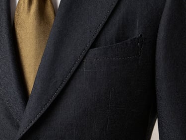 Extreme close-up of a hand-stitched lapel on a charcoal grey blazer, showing the precise thread work and linen texture