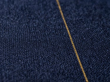 Macro shot of fine navy wool fabric weave, highlighting the tight texture and subtle gold pinstripe, dramatic side lighting
