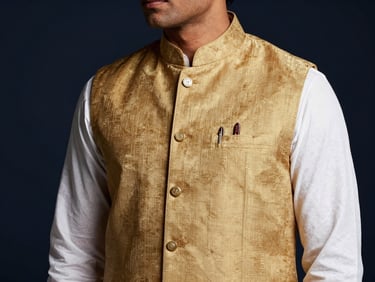 Close-up of a man wearing a textured gold Nehru jacket over a crisp white kurta, side-lit editorial framing