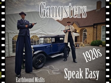 Two 1920s gangsters on stilts holding Tommy guns next to a vintage blue car for a Speakeasy event.