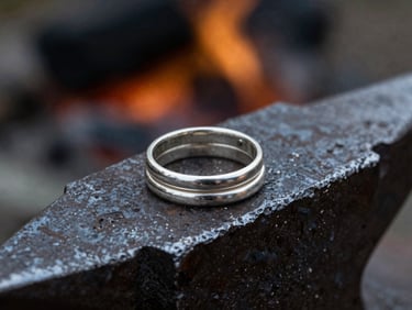 Macro photograph of three thick textured silver wedding bands stacked on a dark iron anvil, cold overcast daylight, high-contrast shadows