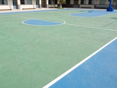 Wide outdoor basketball court of the school, clean green and blue concrete floor, bright sunny day
