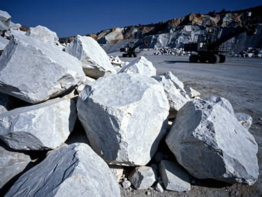 Large white limestone rocks in an industrial quarry, heavy machinery in background, high-contrast cool daylight, deep blue and slate tones, sharp details, wide-angle lens