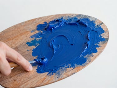Close-up of a hand mixing rich cobalt blue oil paint on a wooden palette, natural north-facing studio light, high texture, sharp focus