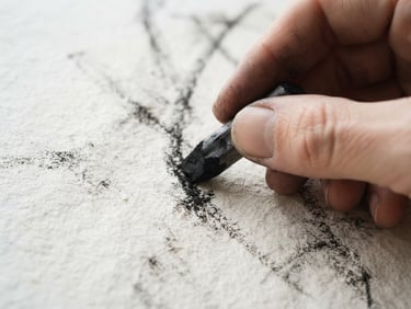 Macro shot of charcoal on heavily textured cotton paper, natural daylight, sharp focus on hand holding drawing tool, minimalist gallery aesthetic, 35mm