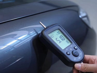 Close-up of a digital paint depth gauge pressed against a clean, polished dark car fender, displaying precise numerical readings, sharp reflections, cool blue lighting