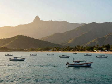 Wide environmental shot of Santa Marta bay at dawn, fishing boats on calm turquoise water, Sierra Nevada foothills rising in the background under golden-hour haze, no people in frame
