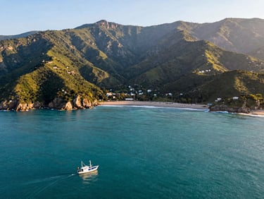Wide shot of Santa Marta bay from above, turquoise water meeting green Sierra Nevada foothills, a small fishing boat in the foreground, warm morning light