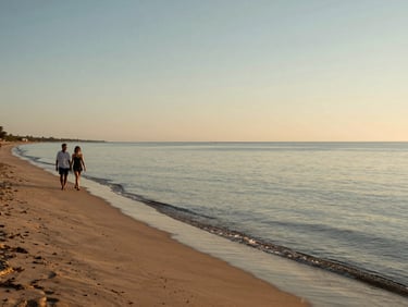Coveñas beach at late afternoon, calm shallow water, a couple walking along the shoreline to the left, wide open sky, warm amber light on the sand