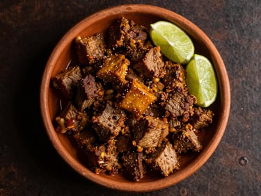 Overhead flat-lay of a kilo of golden pork carnitas served in a clay dish with lime wedges