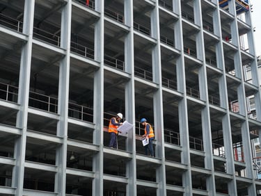 Wide environmental shot of structural steel retrofitting on a commercial building facade in Singapore, engineers in orange vests reviewing blueprints