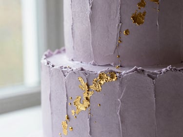 An elegant bespoke birthday cake with modern textured frosting and gold leaf accents, close-up shot.