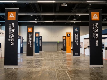 Wide environmental shot of an expo hall interior, branded vertical banners and directional signage installed along the perimeter, soft tungsten overhead lighting, no people in frame, shot from mid-aisle looking toward the back wall