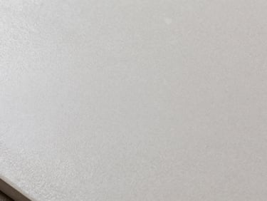 Extreme close-up of large-format porcelain tile surface under studio strobe lighting, showing fine grain texture and matte glaze finish, cool neutral tones, architectural product flatlay