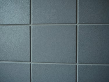 Close-up of a tiled wall section with textured matte finish, grout lines precise and even, cool diffused studio light emphasising surface relief and material consistency, no people