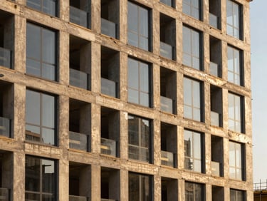 Modern commercial building facade under construction, exposed concrete pillars and glass panels, warm golden hour light, architectural photography