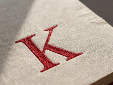 Macro detail of a linen book jacket with deep debossed crimson lettering, soft directional window light with natural shadows