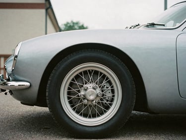 Close-up of a classic silver sports car's wire wheel, soft overcast daylight, architectural framing, 35mm film.