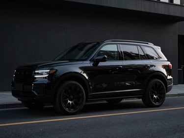 Sleek black armored SUV, low-profile, parked on a city street at dusk, cinematic shadows, no visible branding.
