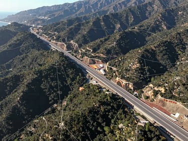 Wide-angle aerial view of a coastal highway infrastructure project in Chile, crisp daylight, precise geographic mapping lines overlaid on the landscape.