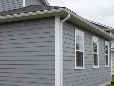 Wide environmental shot of a residential exterior facade, freshly painted gray siding with white trim detail, overcast daylight, no people, clean gutters and downspouts visible