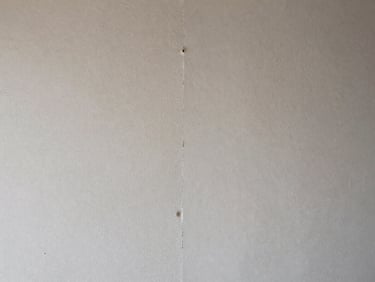 Side-by-side close-up of drywall surface — left half showing a patched and sanded repair scar, right half freshly primed and smooth, harsh raking light revealing texture difference