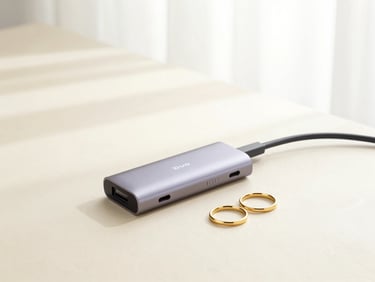 Bright high-key product photography of a sleek USB-C hub and elegant gold rings arranged on a warm cream desk, soft natural window light, 50mm lens