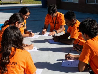 Diverse community college students actively engaged in a workshop, high-contrast outdoor shadows, vibrant safety orange accents, candid action, 35mm