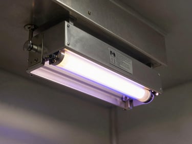 UV sterilization lamp unit installed in a ship's galley pantry, glowing ultraviolet tube visible, stainless steel surfaces around it, tight framing showing spec label on housing